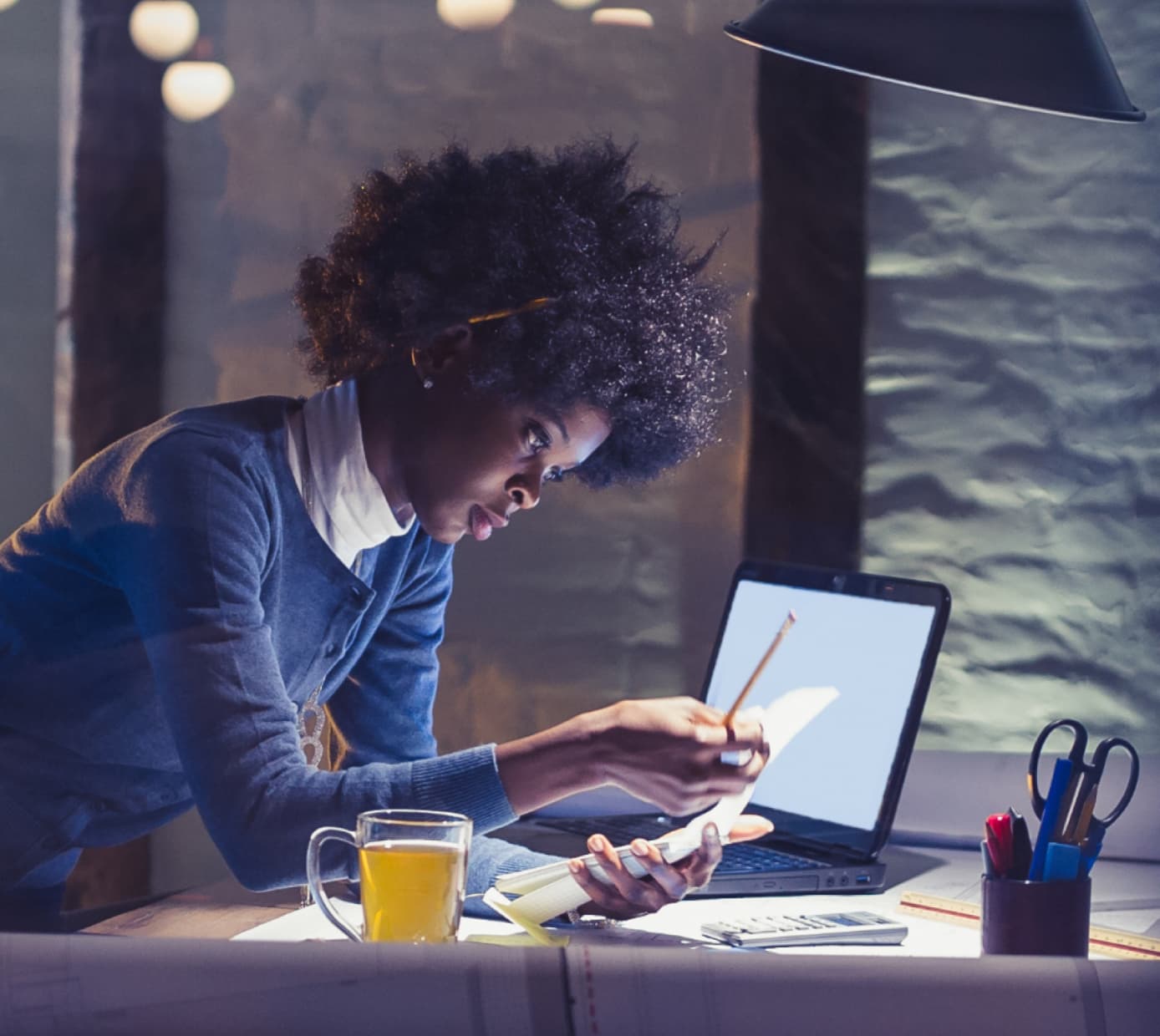 一名女性专家独自在空旷的办公室工作，身旁放着一杯茶和一台笔记本电脑。